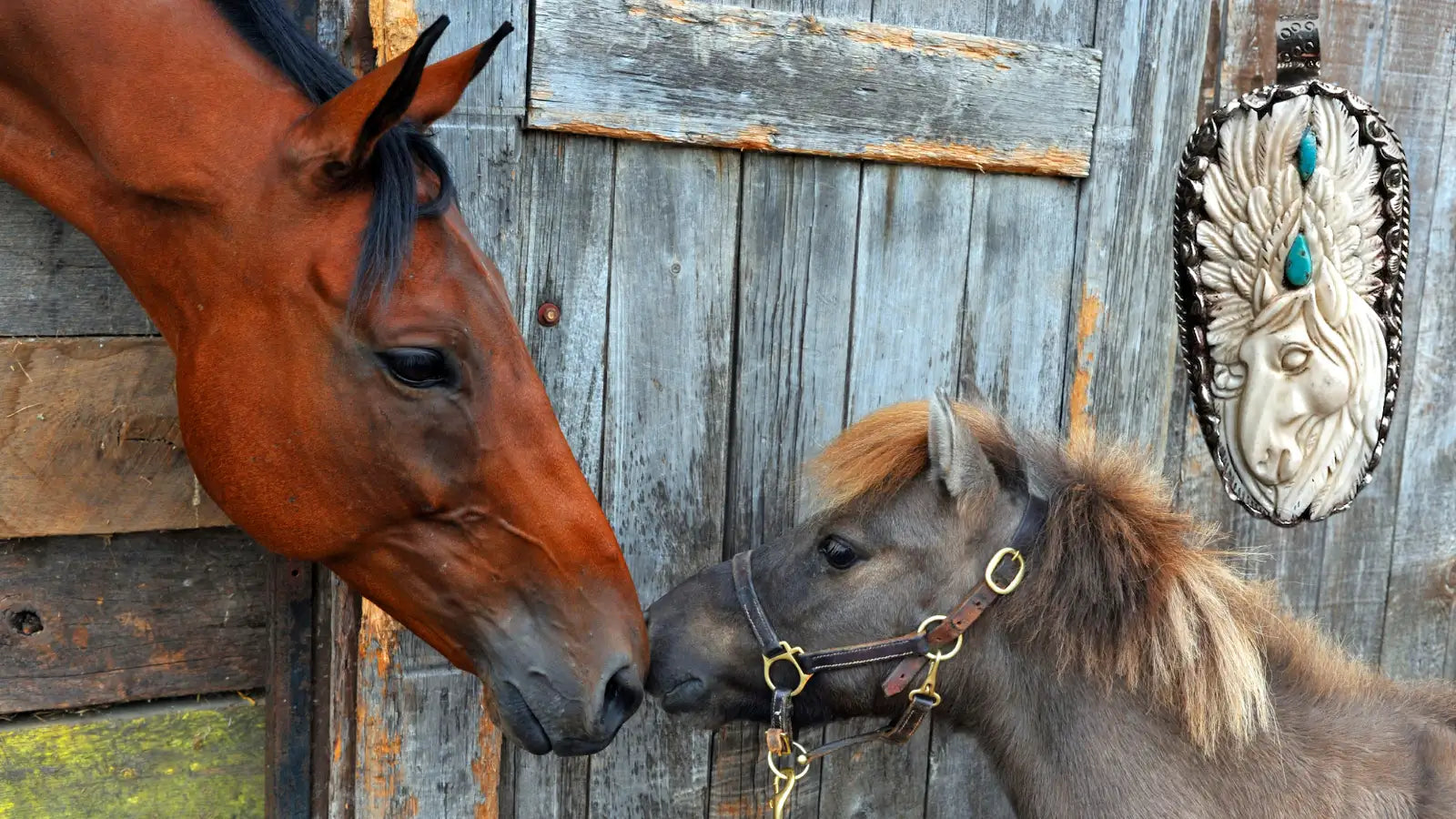 A silver-toned, intricately detailed native american-style pendant featuring a carved face with turquoise inlays and an ornate feather design.